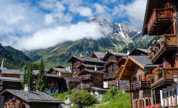 Resort buildings in a green area, with alps in the background